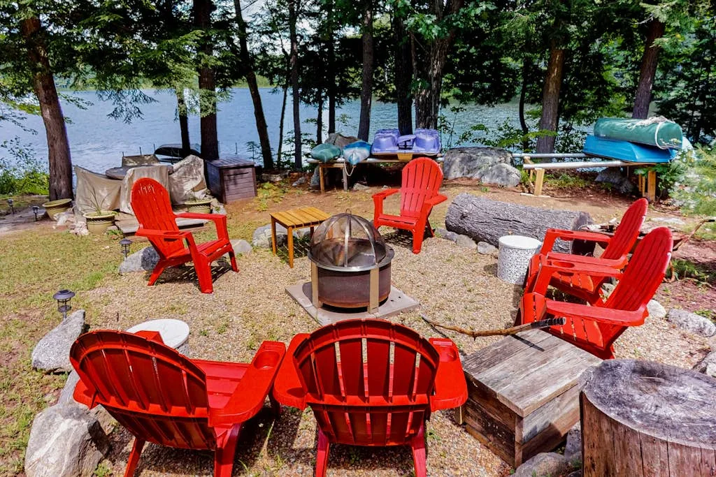 An outdoor lakeside seating area with red chairs arranged around a fire pit.