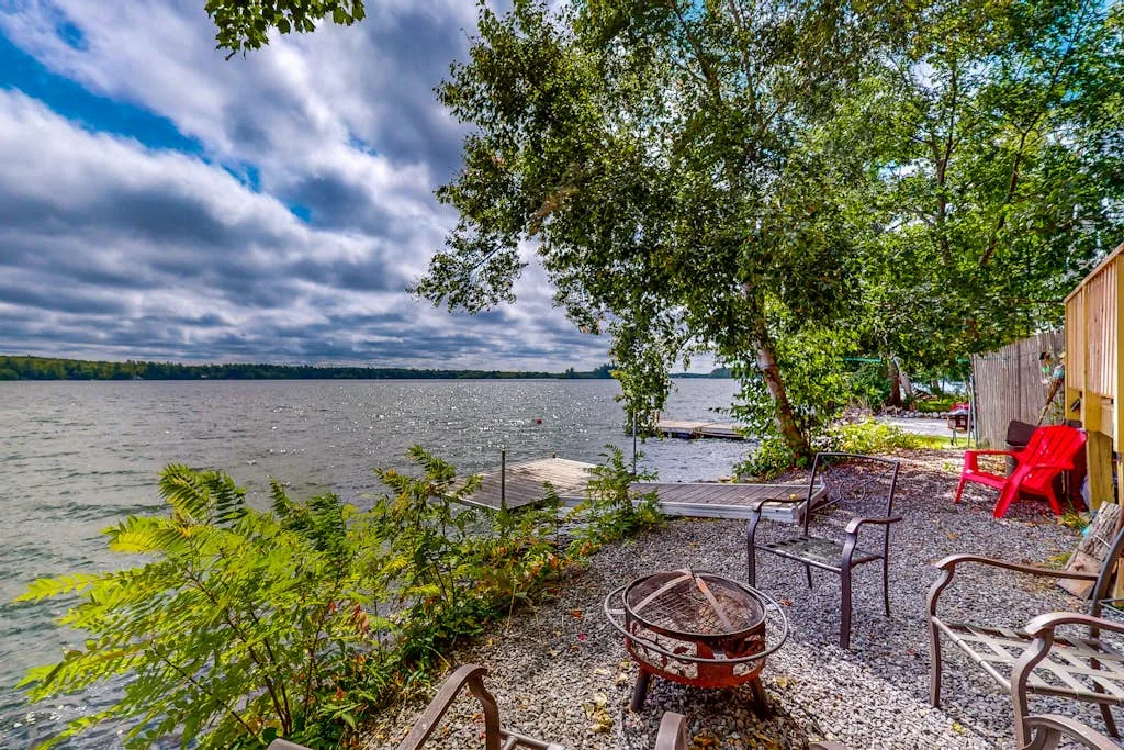 A gravel seating area beside a lakeshore, shaded by trees.