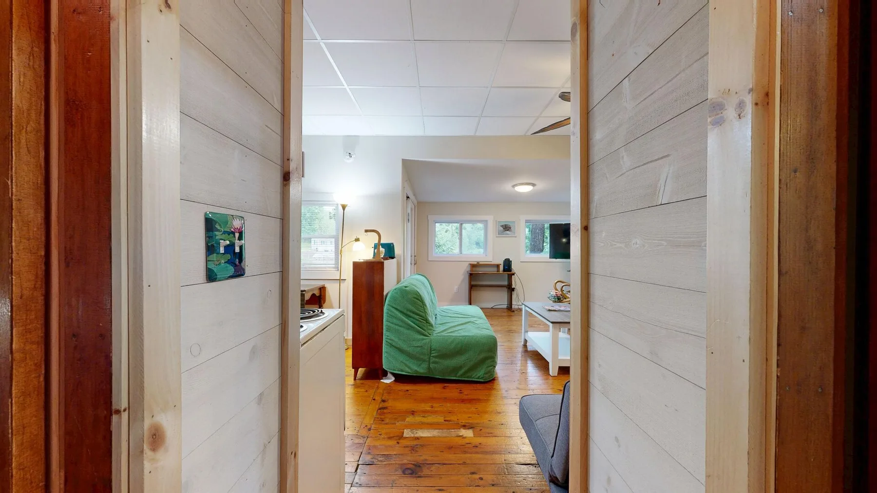 A living area with green seating and a wooden floor, viewed through an open doorway.