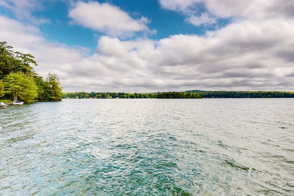 A lake stretches toward a tree-lined shore beneath a cloudy sky.