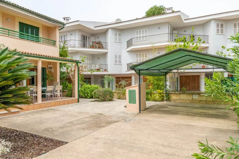 A residential courtyard with a paved driveway, greenery, and a covered parking area.