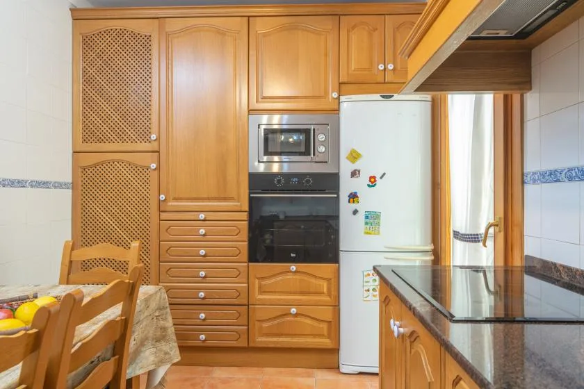 A warm-toned kitchen with wooden cabinets, built-in appliances, and a dining table.