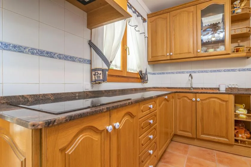 A tiled kitchen with wooden cabinets, a countertop, and a curtained window.