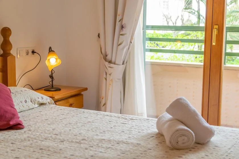 A bedroom with a bed beside a lit bedside lamp and a curtained window.