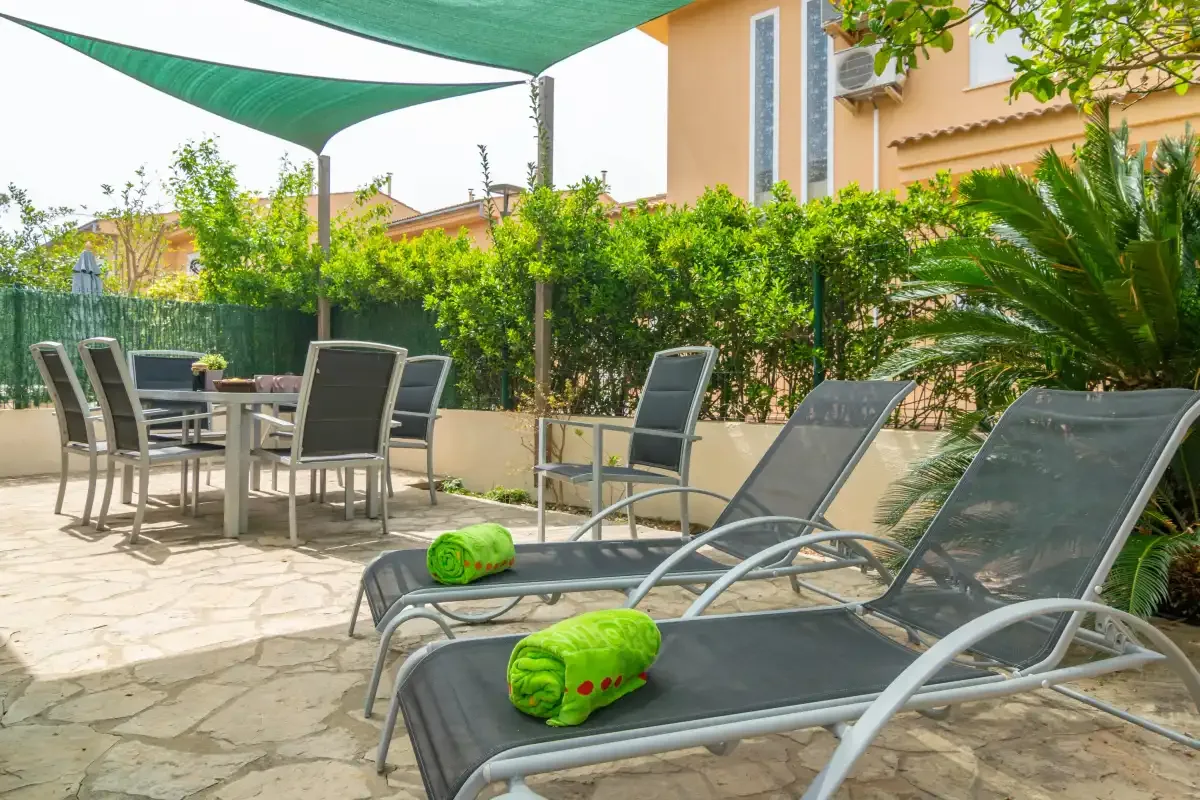 A sunny outdoor patio with lounge chairs, a dining table, and greenery.