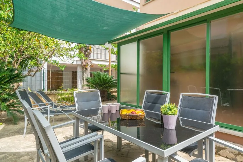 A patio seating area with a glass table beneath a green shade canopy.