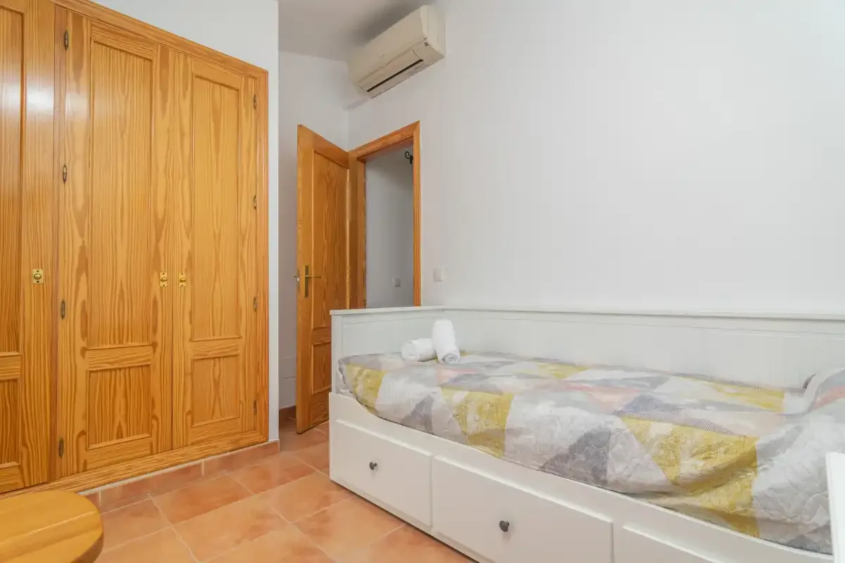 A bedroom with a bed, built-in wooden wardrobes, and an open door.