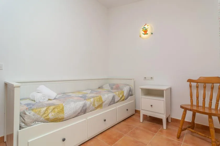 A bedroom with a single bed, a bedside cabinet, and a wooden chair.
