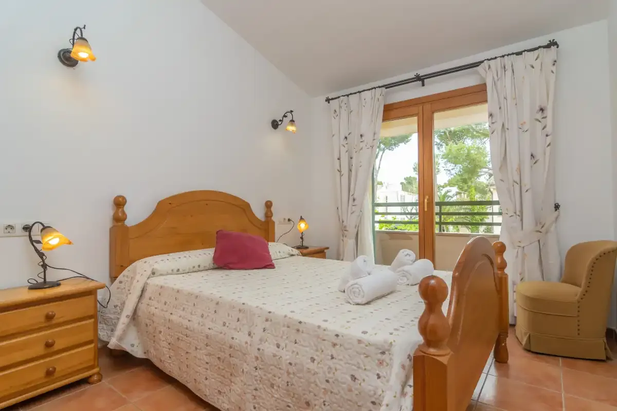 A bedroom with a wooden bed, bedside drawers, and glass doors opening onto a balcony.