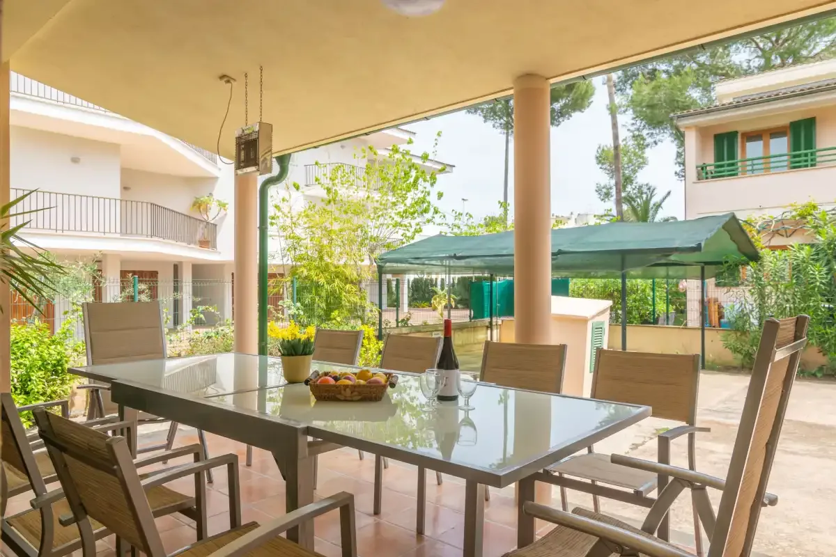 A covered outdoor dining area with a table and seating overlooks a garden.