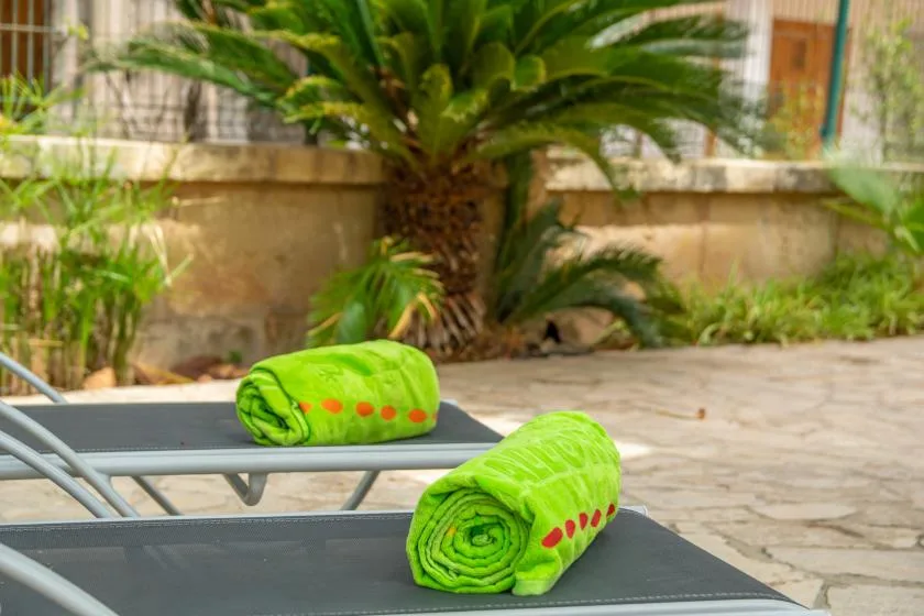 Outdoor patio loungers with bright green towels sit beside a leafy garden.