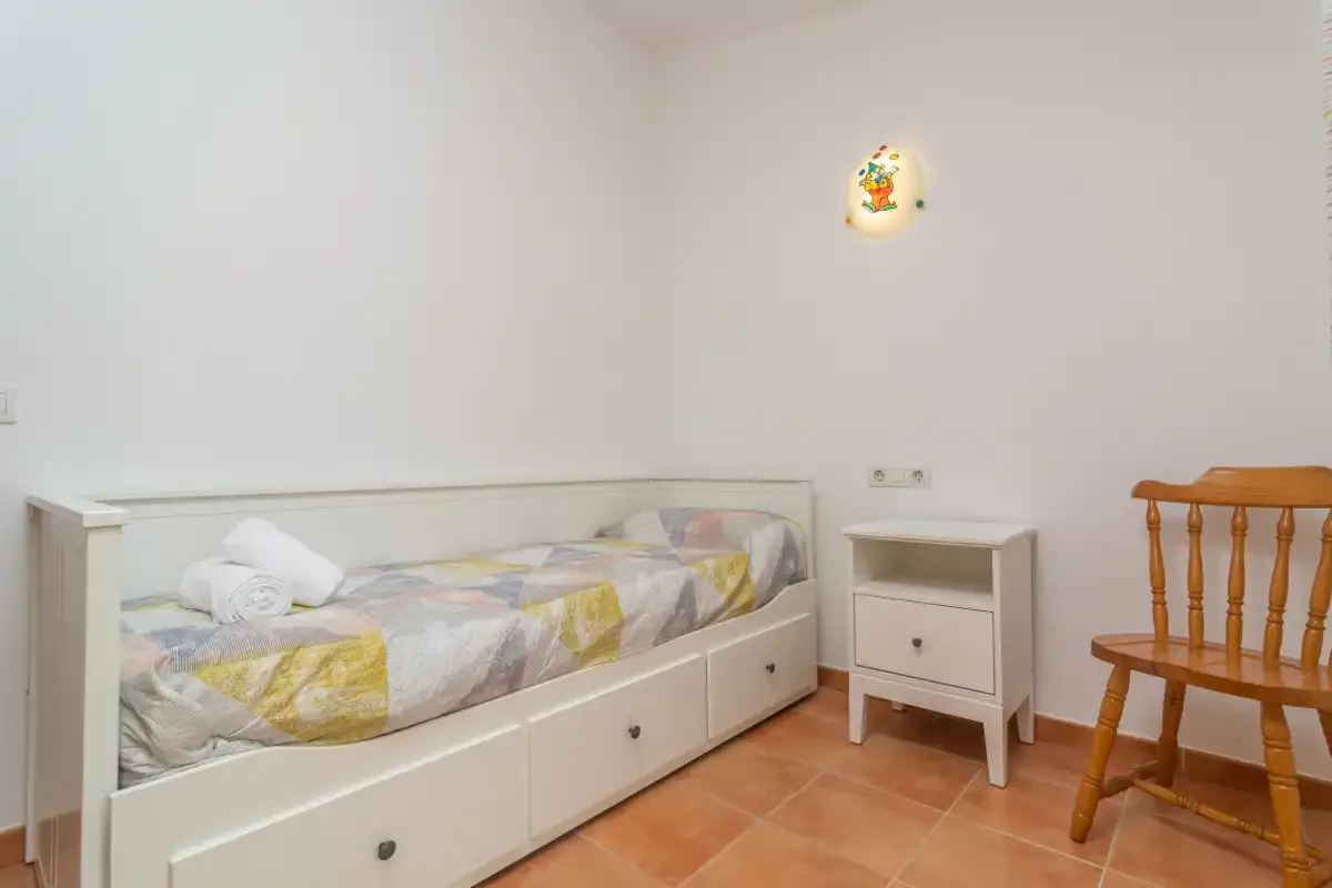 A bedroom with a single bed, a small bedside table, and a wooden chair.