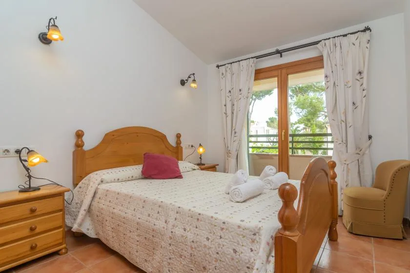 A bedroom with a wooden bed, bedside table, and glass doors opening onto a balcony.