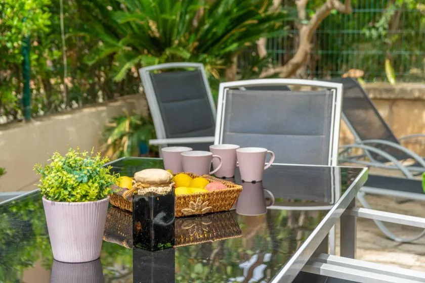 An outdoor patio table with cups, fruit, and seating surrounded by greenery.