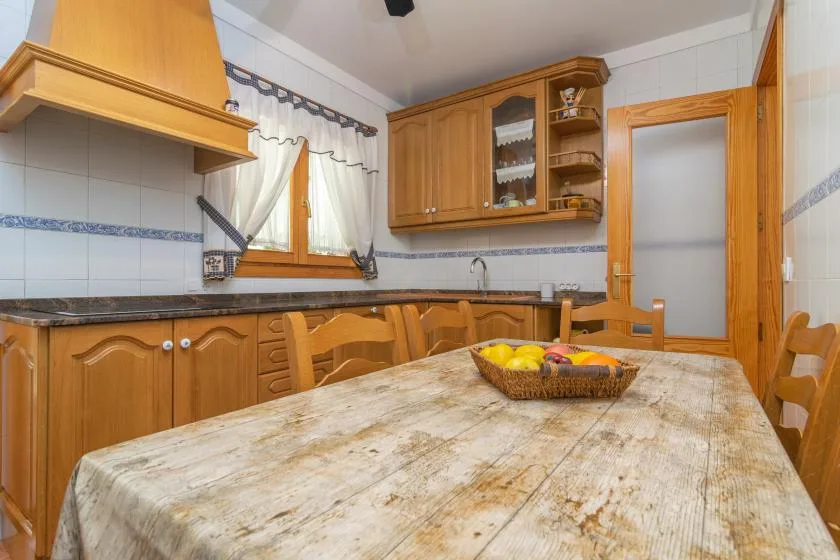 A tiled kitchen with wooden cabinets, a window, and a dining table.