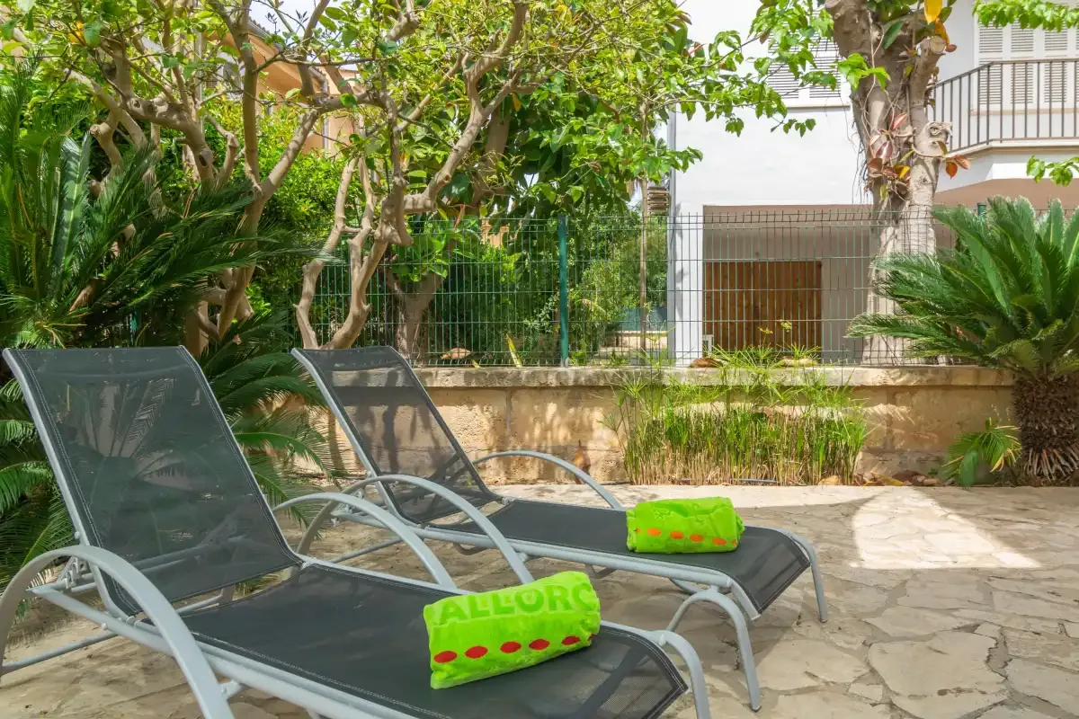 A garden patio has lounge seating beside leafy plants and a stone walkway.
