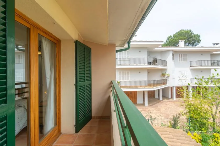 A balcony with green railings overlooks a courtyard and a nearby building.