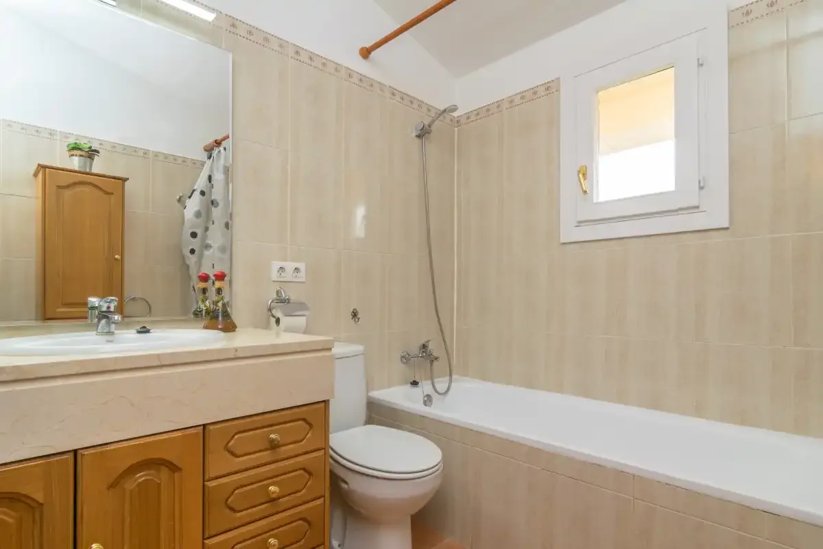 A tiled bathroom with a bathtub, shower, toilet, and wooden vanity.