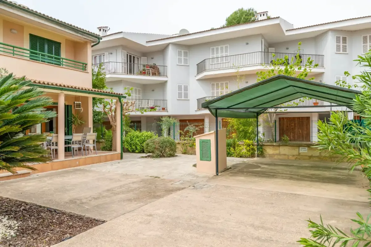 A courtyard between residential buildings, with a covered parking area and patio seating.