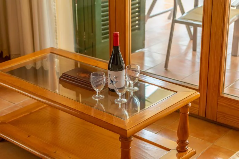 A glass-topped wooden table holds a bottle of wine and two glasses.