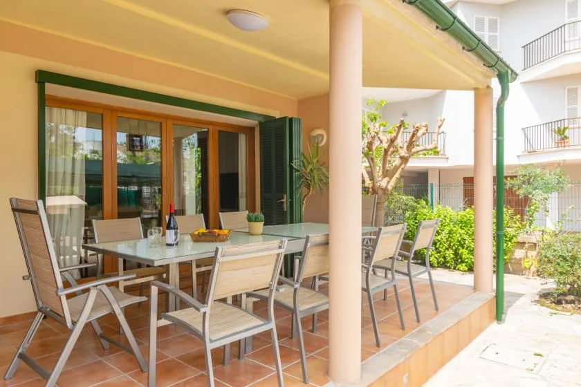 A covered patio has a dining table and seating beside glass doors.