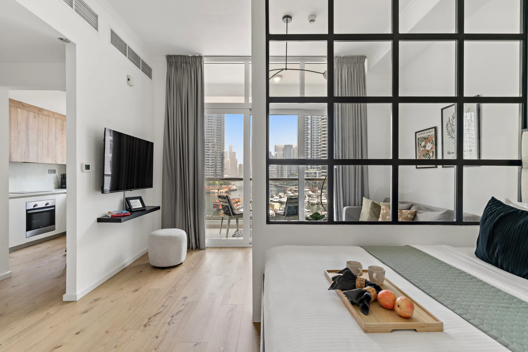 Un dormitorio luminoso con una cama, una división de vidrio con marco negro y vistas a la ciudad.