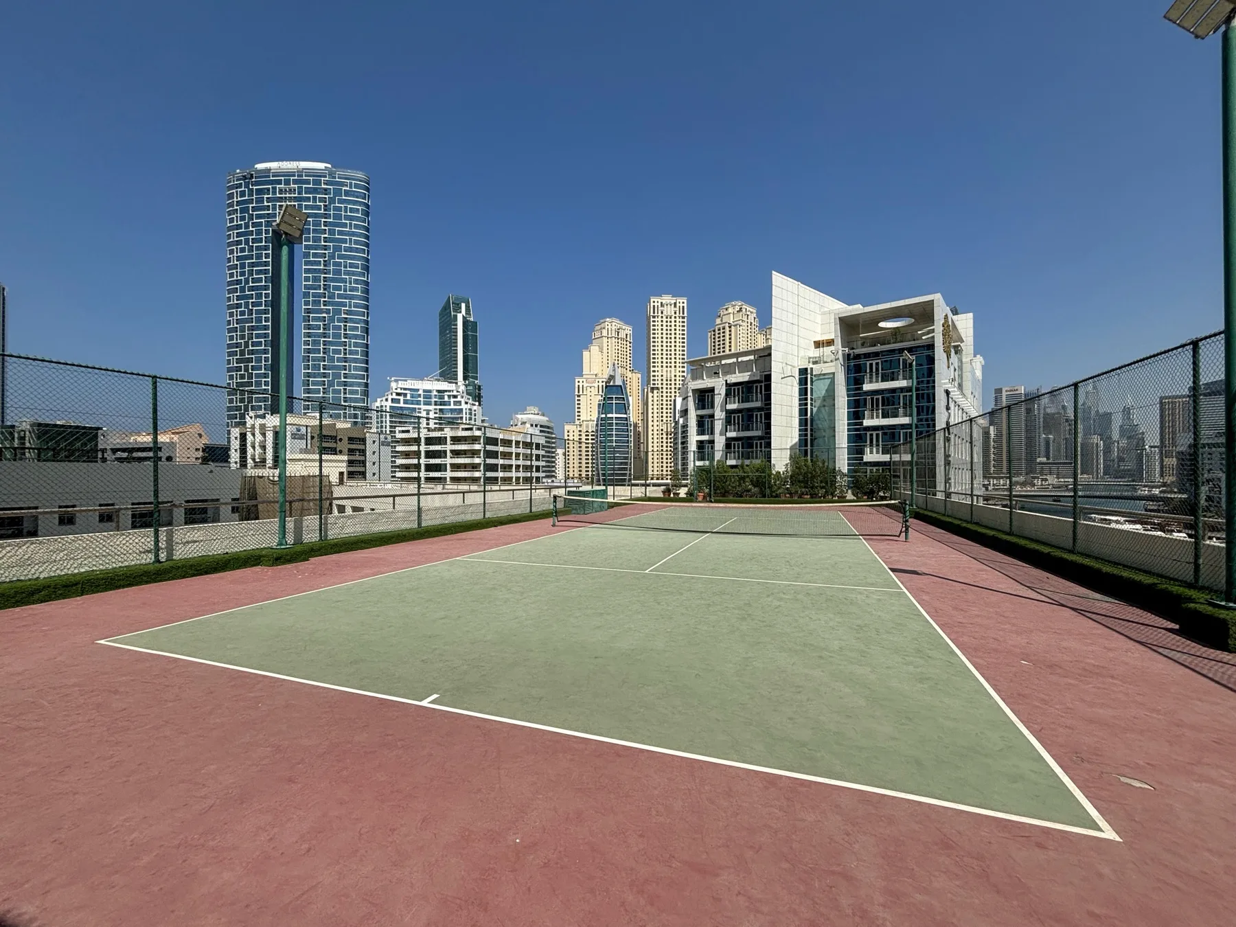 Una cancha de tenis al aire libre da a un conjunto de edificios urbanos.