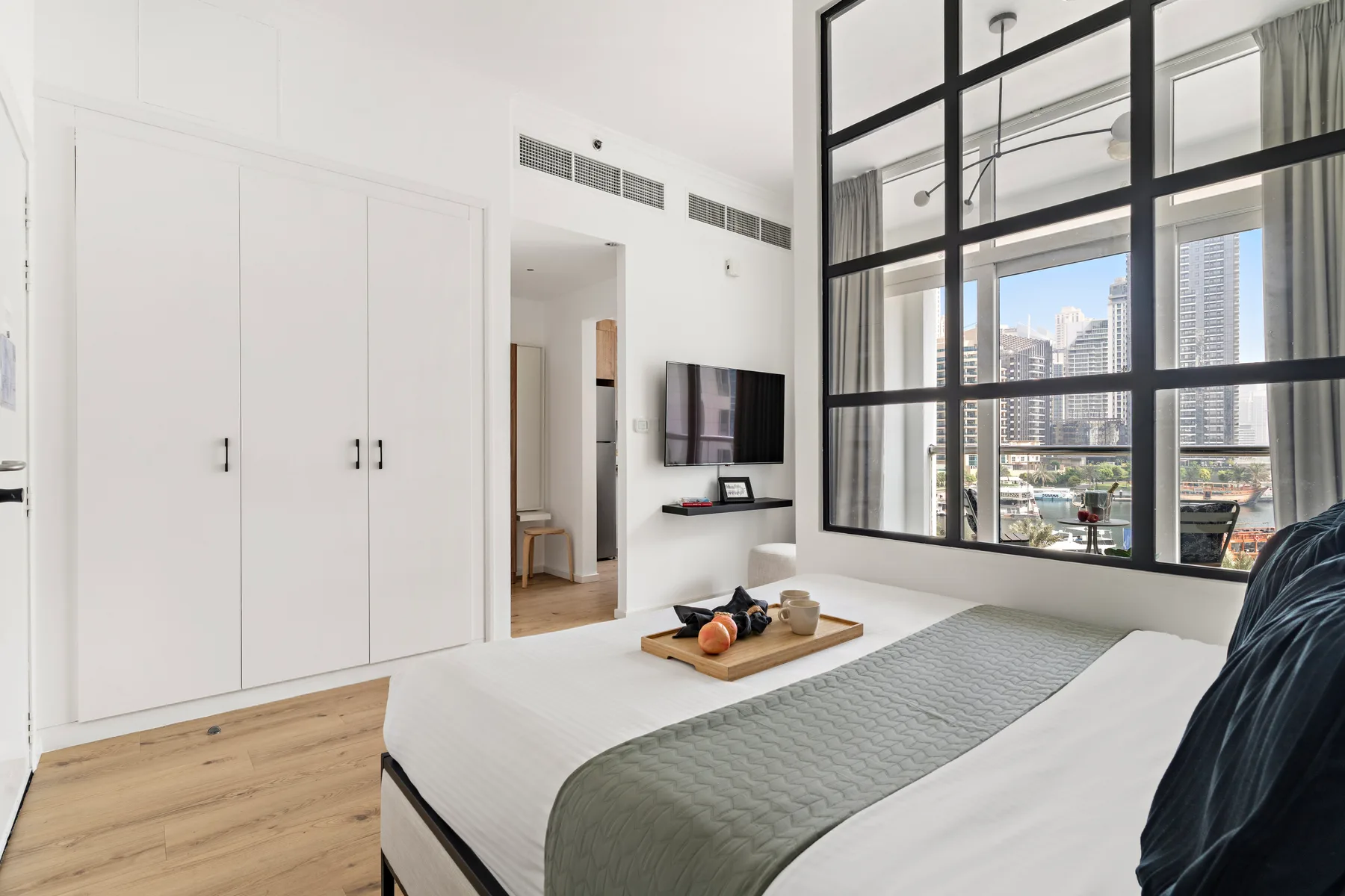 Un dormitorio luminoso con una cama, armarios empotrados y grandes ventanas con marcos negros.