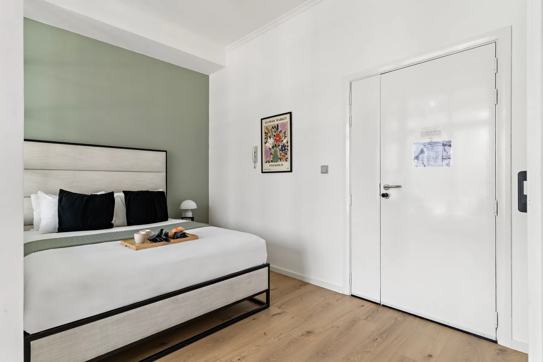 Un dormitorio con una cama bien tendida, una pared verde pálido y una puerta blanca.