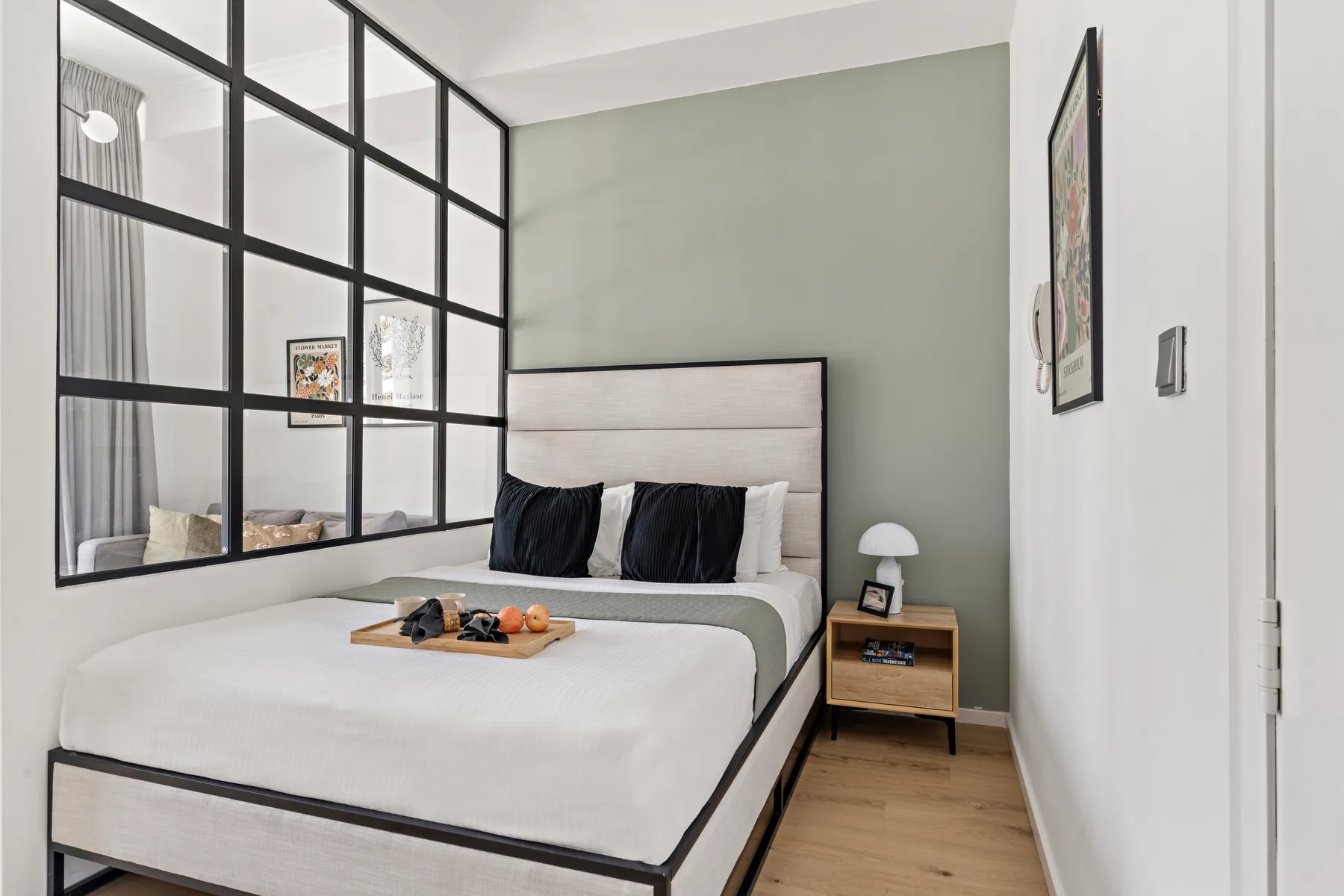 Un dormitorio con una cama tendida junto a una ventana interior de marco negro.