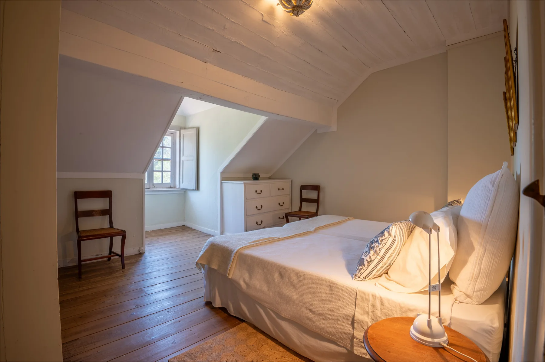 Un dormitorio luminoso con una cama, suelo de madera y techo inclinado.