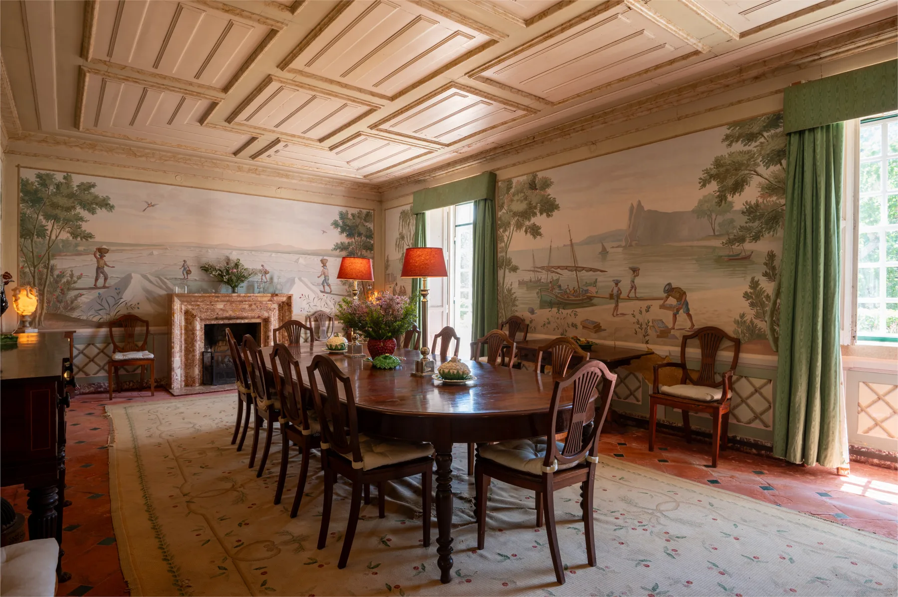 Un comedor formal con una larga mesa de madera y escenas pintadas en las paredes.