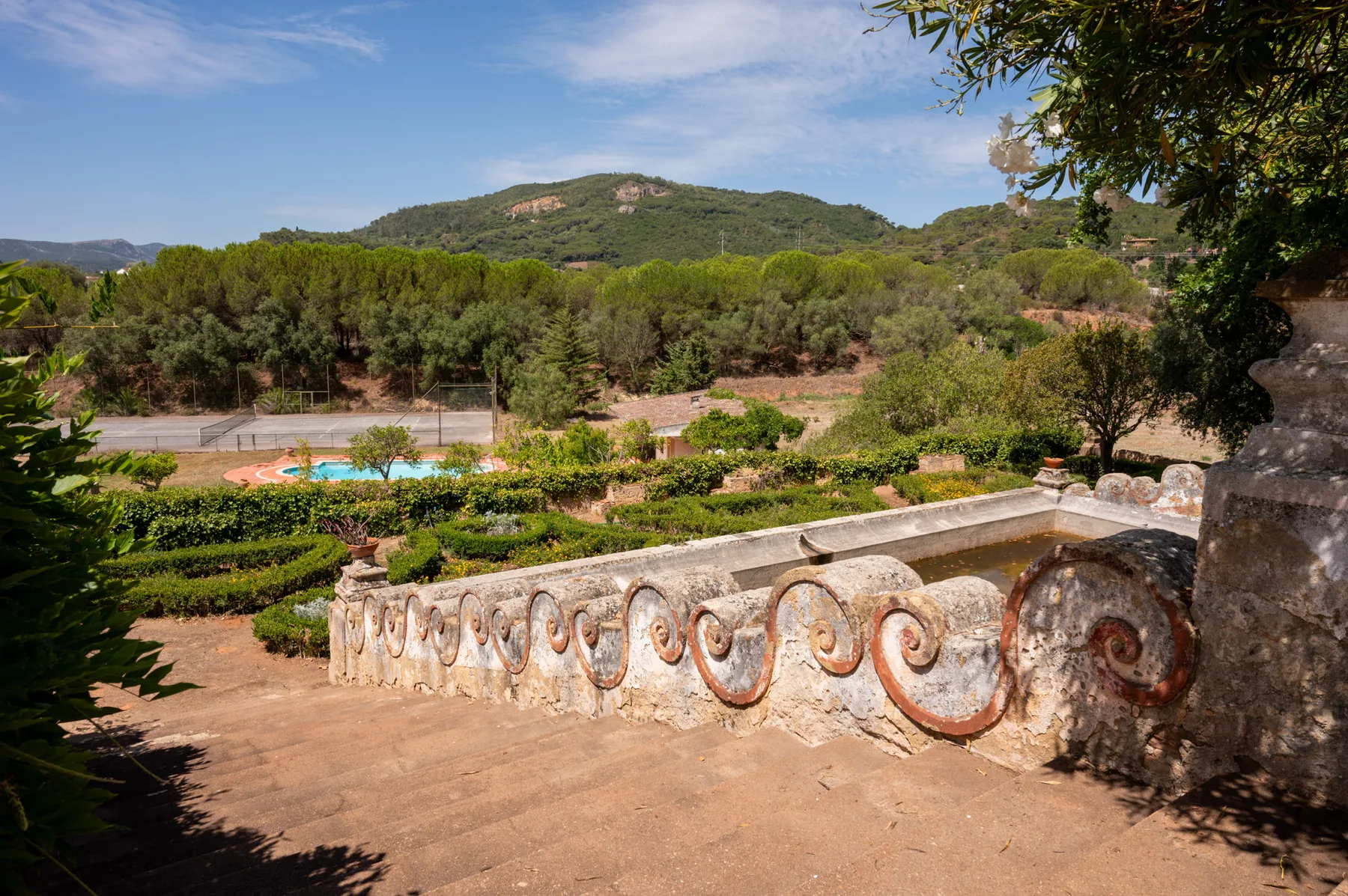 Una terraza ajardinada da a jardines, una piscina y colinas boscosas.