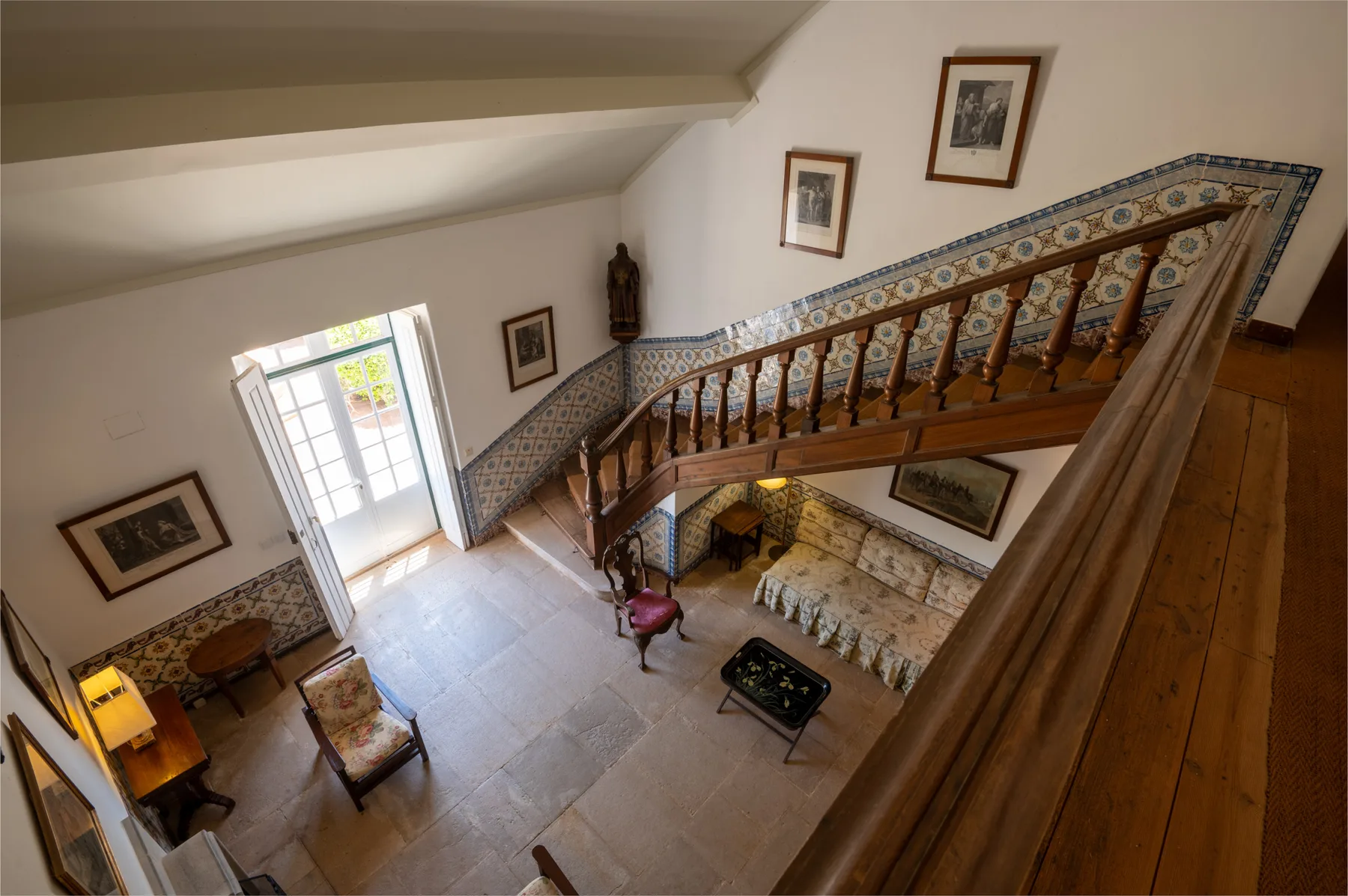 Un rellano interior de escalera da a una sala de estar con azulejos y una ventana luminosa.