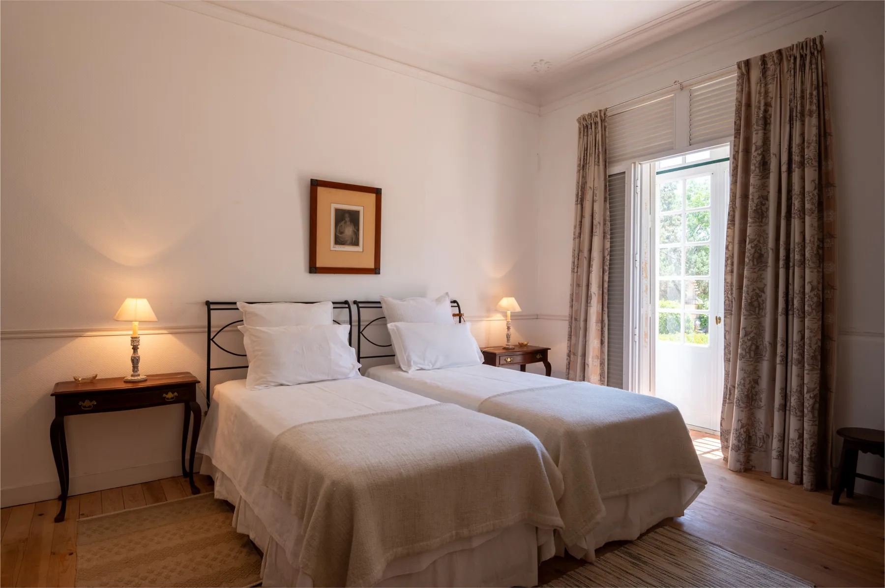 Un dormitorio con camas individuales, mesillas y una puerta acristalada hacia el exterior iluminado.