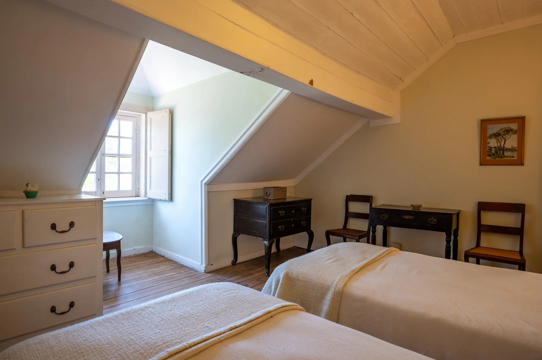 Un dormitorio abuhardillado con camas, una cómoda y un escritorio bajo el techo inclinado.