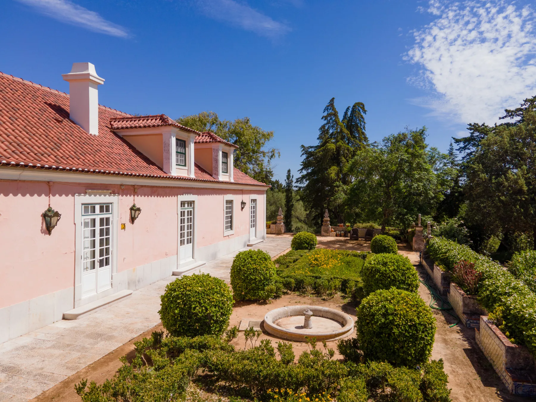 Una casa rosa da a un jardín con arbustos recortados y una fuente circular.