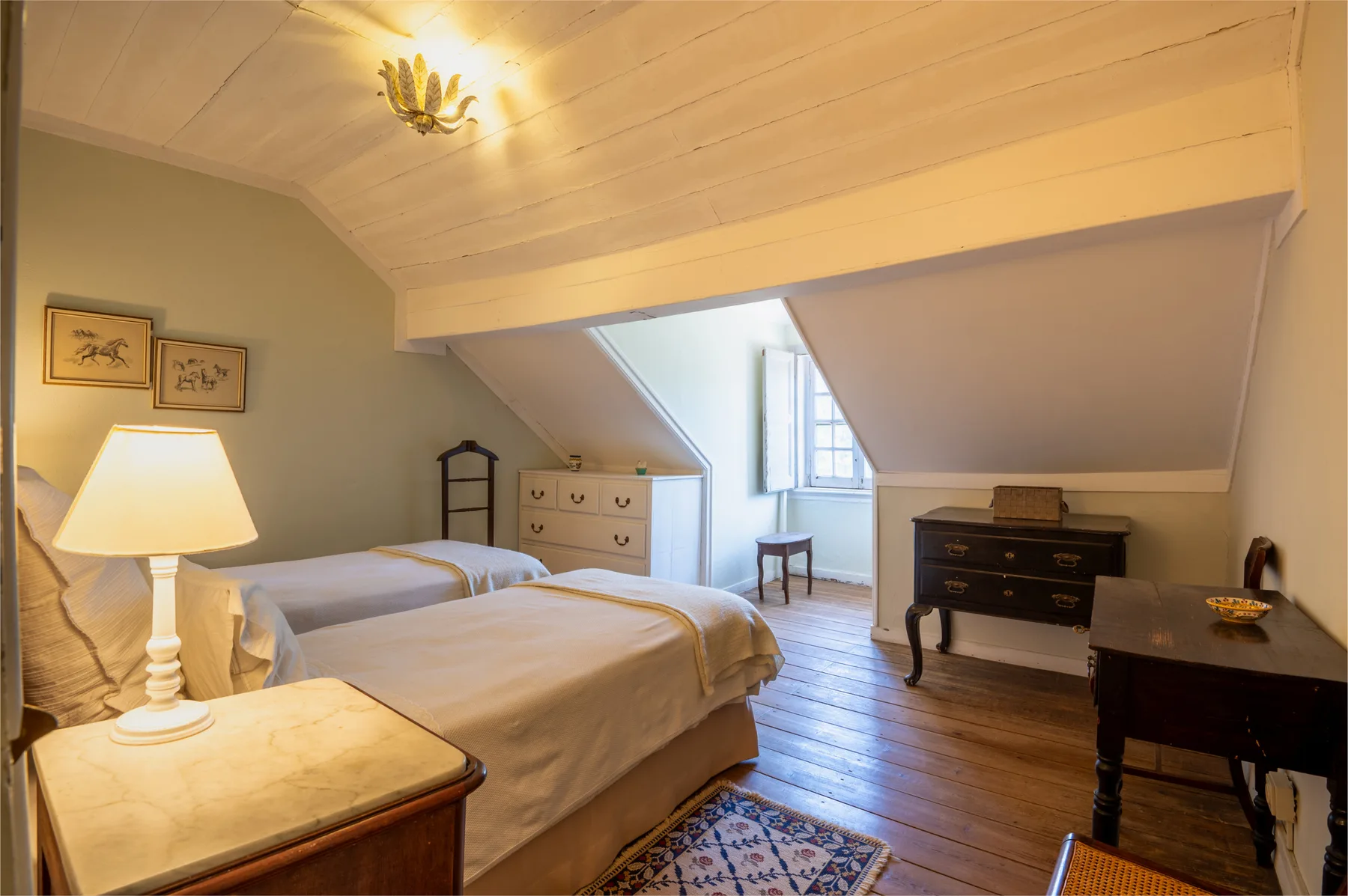 Un dormitorio abuhardillado luminoso con dos camas y una ventana bajo el techo inclinado.