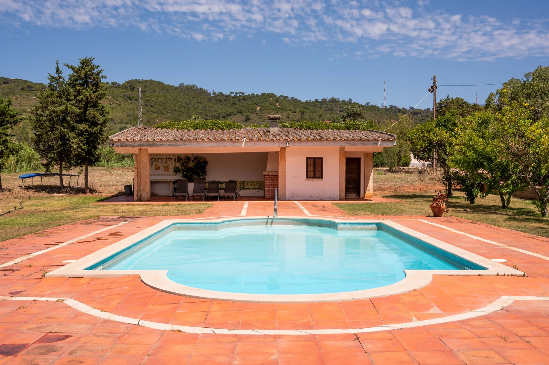 An outdoor swimming pool sits in front of a low building in a rural landscape.
