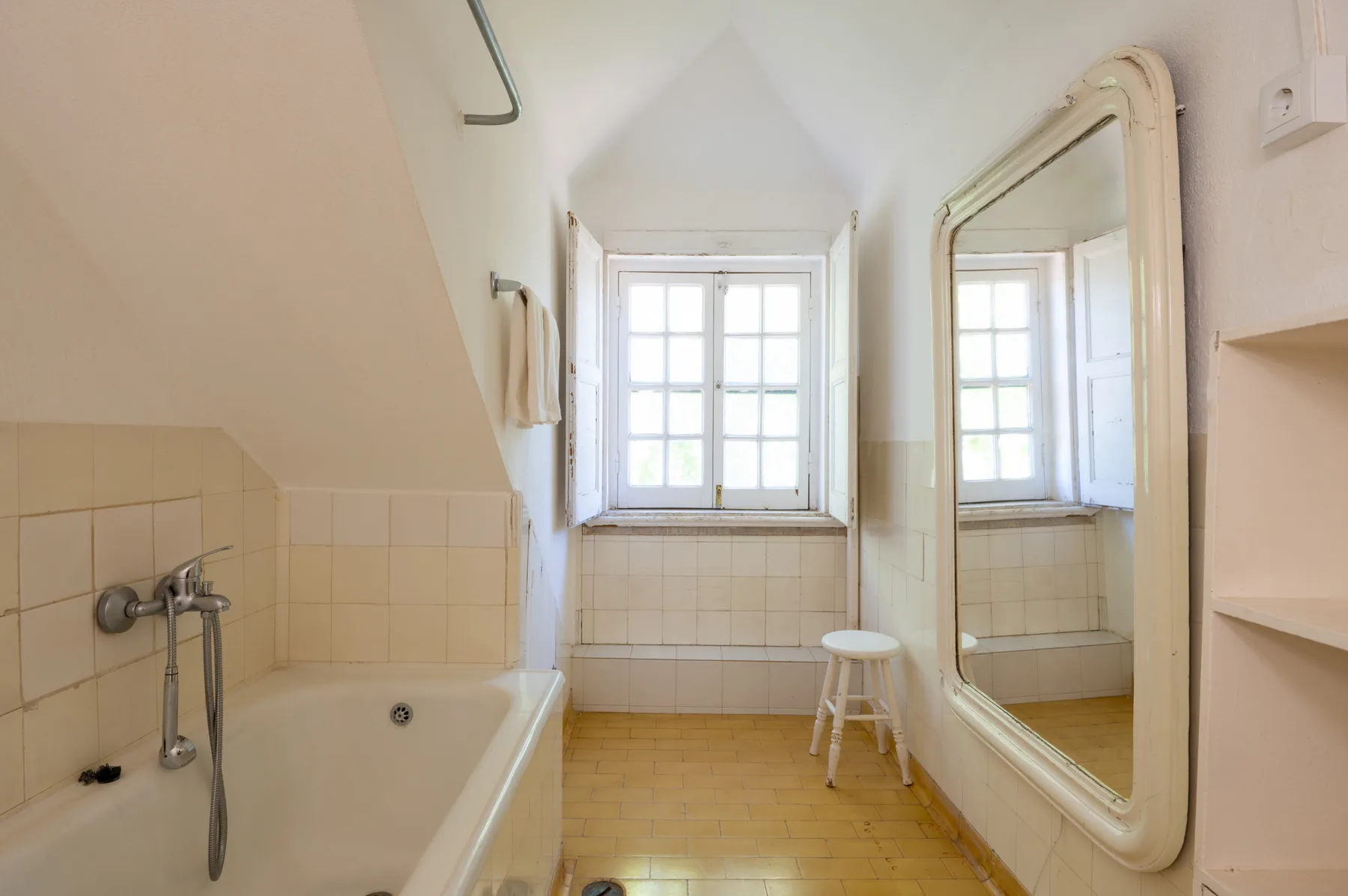 Un baño luminoso con bañera, ventana y un espejo grande en la pared.