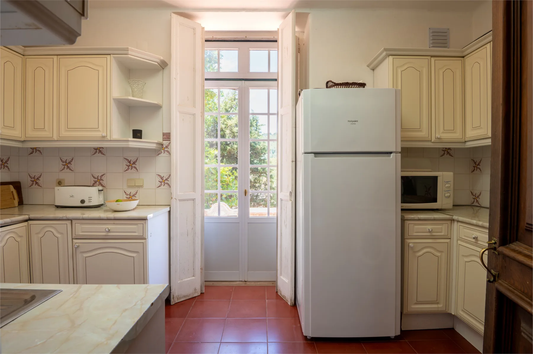 Cocina con armarios color crema y un refrigerador alto junto a puertas acristaladas.
