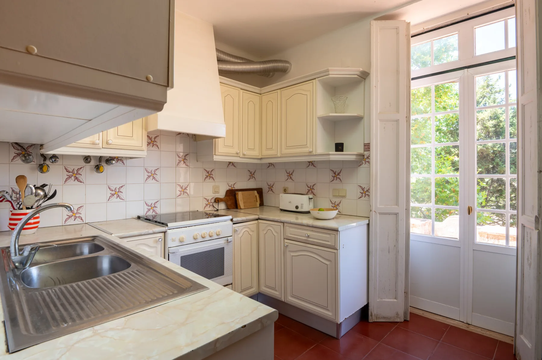 Una cocina luminosa con armarios color crema, azulejos y puertas de vidrio.