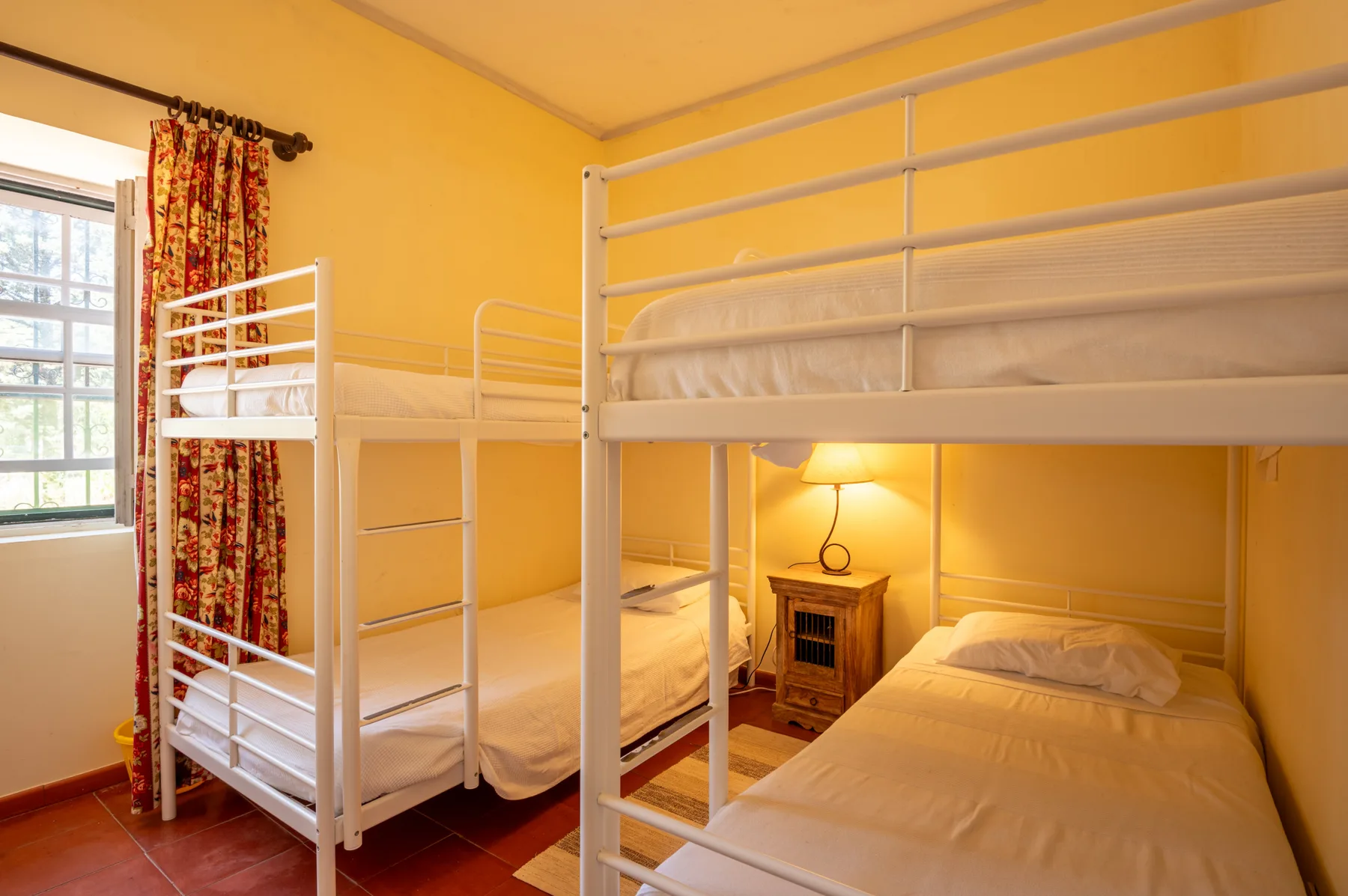Un dormitorio con literas blancas y una lámpara de noche junto a la ventana.