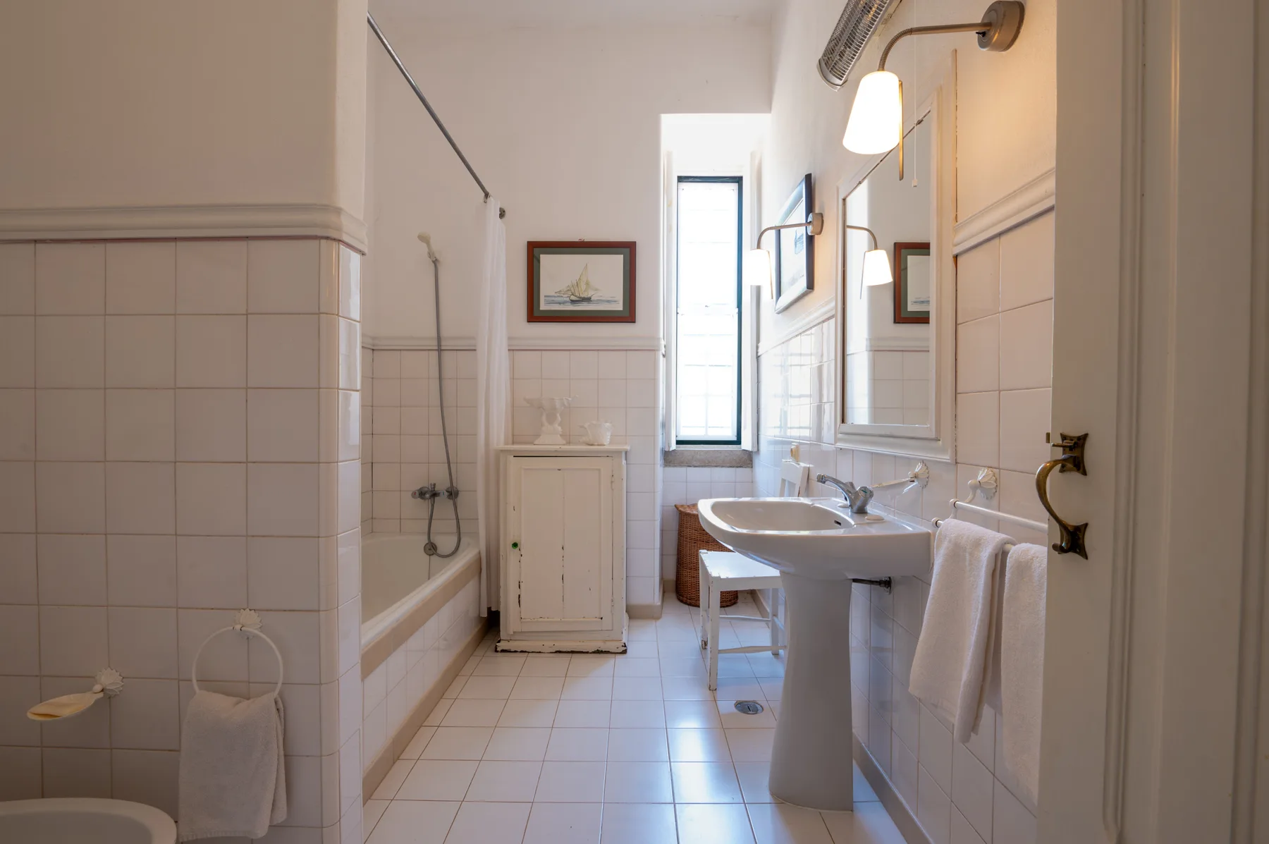 Un baño luminoso con azulejos, bañera y lavabo con pedestal.