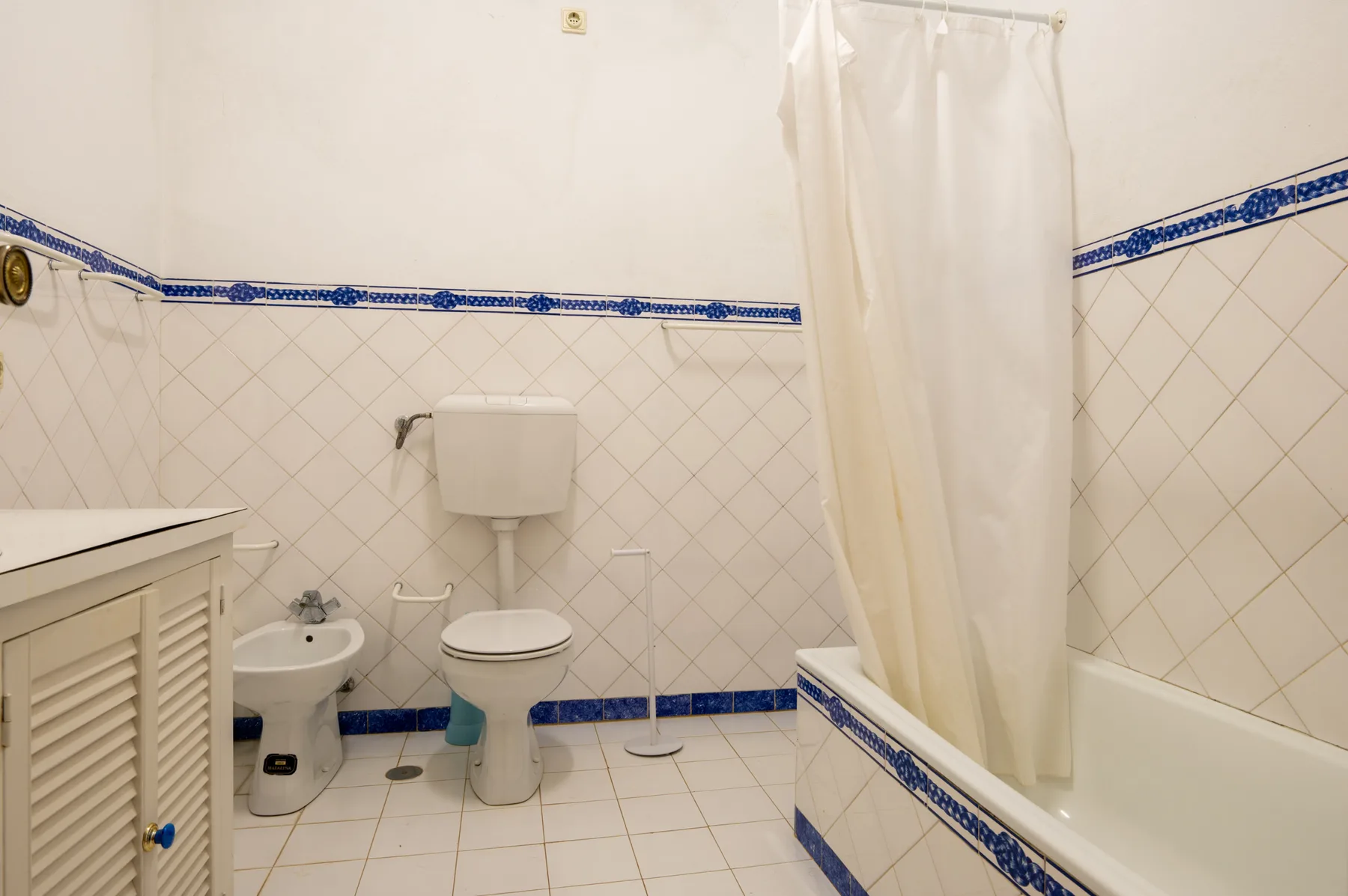 Un baño alicatado con inodoro, bidé y bañera detrás de una cortina de ducha.