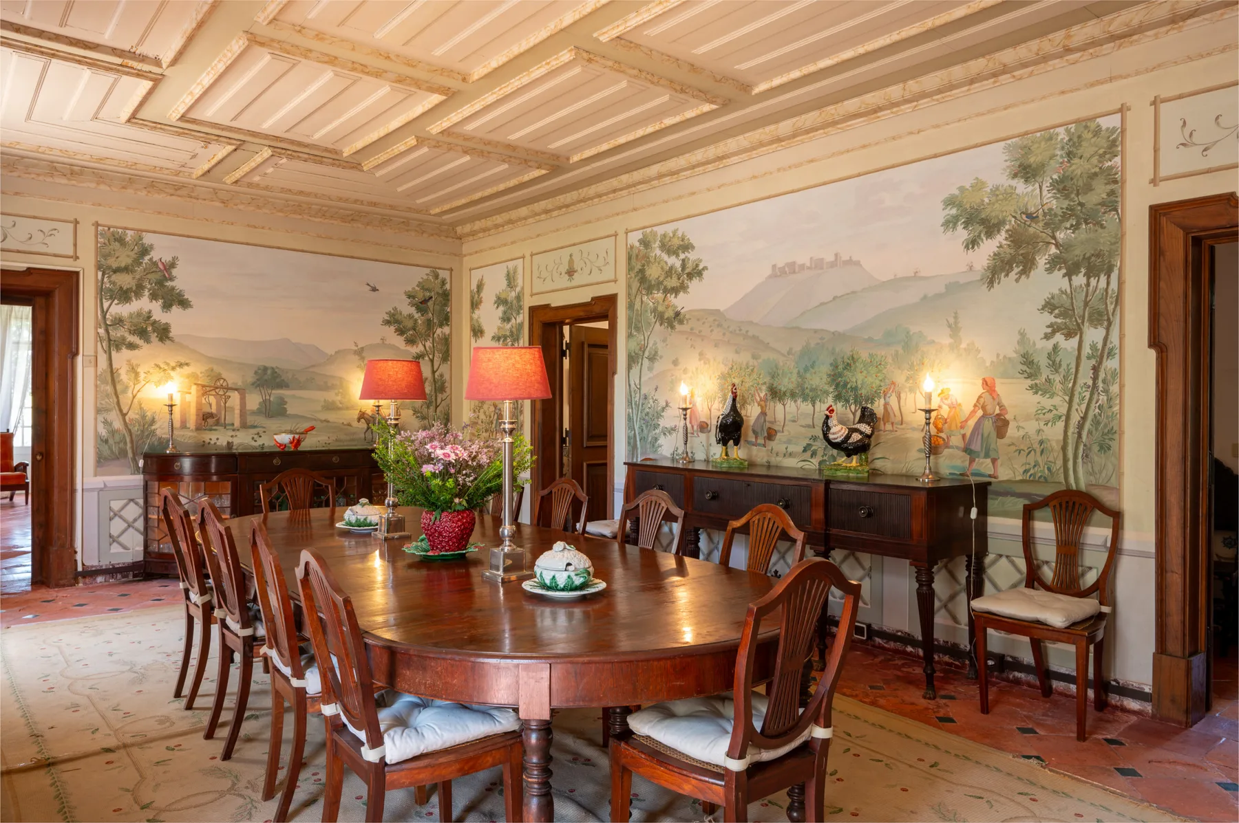 Un comedor formal con una larga mesa de madera y murales pintados en las paredes.