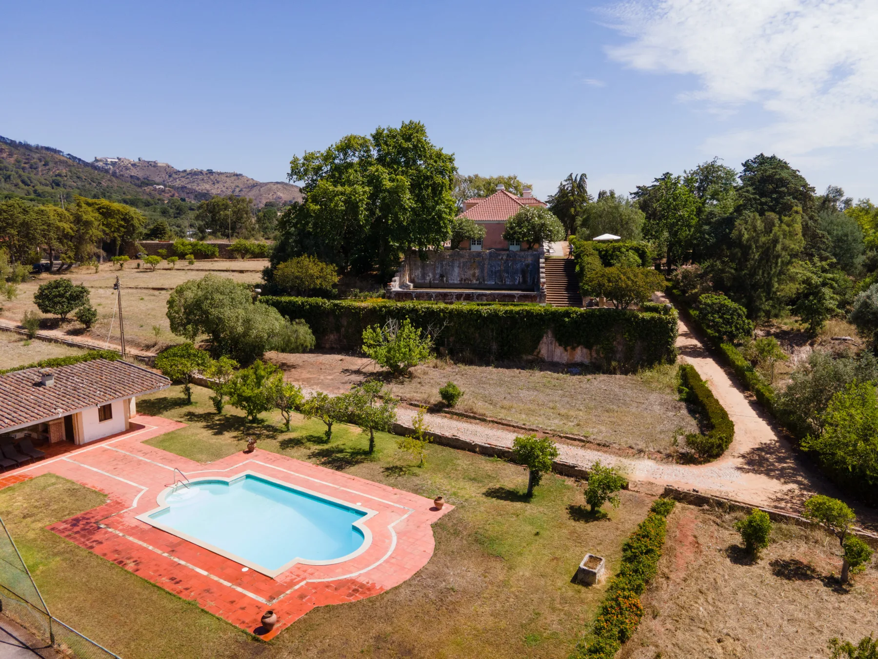 Vista aérea de una piscina y terrenos ajardinados con una casa al fondo.