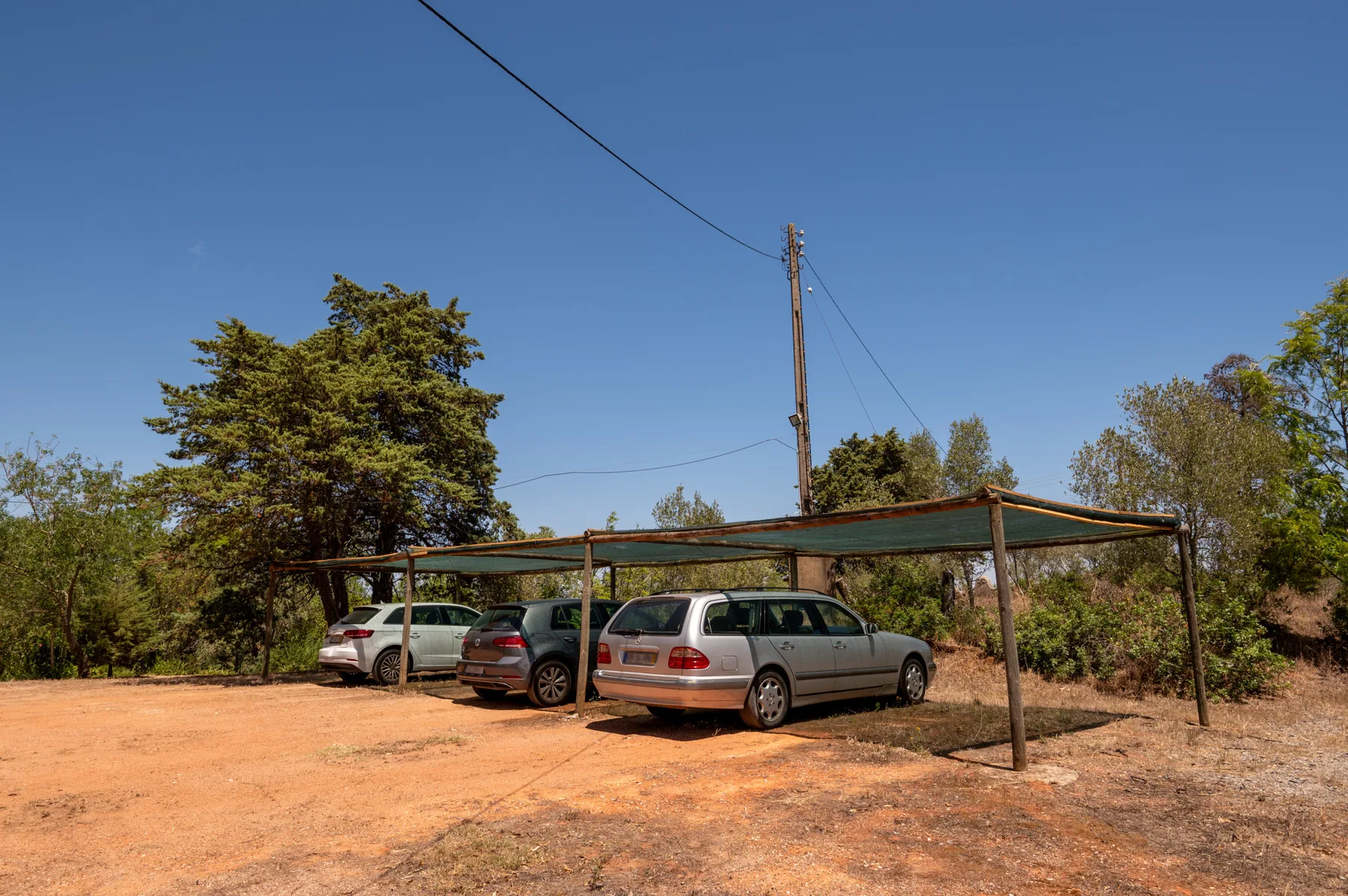 Una zona de estacionamiento de tierra con varios coches bajo un toldo sencillo.