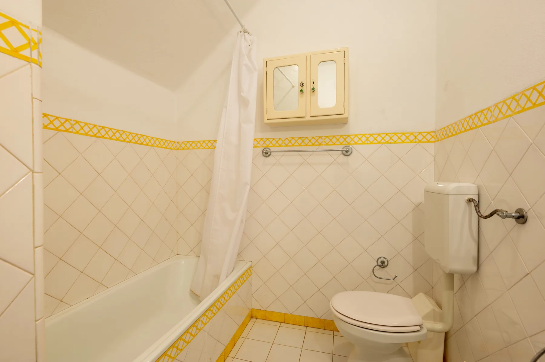 Un baño alicatado con bañera, cortina de ducha e inodoro.