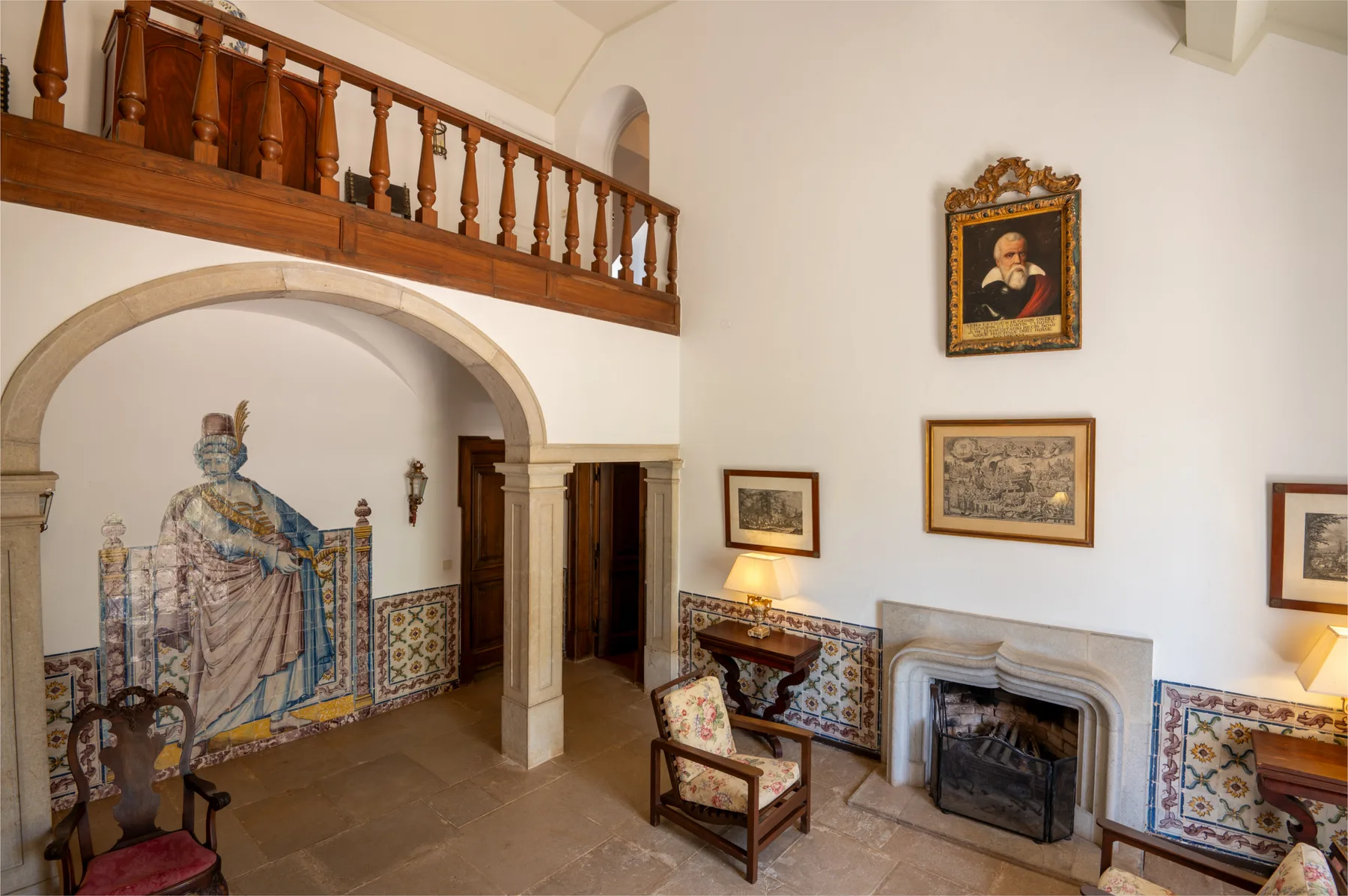 Interior con un mural de azulejos bajo un balcón de madera y una chimenea.